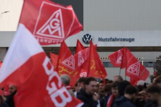 Operários com bandeiras da IG Metall, que é o sindicato de metalúrgicos da Alemanha, protestam em frente à fábrica da Volkswagen em Hanover. Trabalhadores da indústria automobilística fazem protesto em todo o país nesta segunda-feira