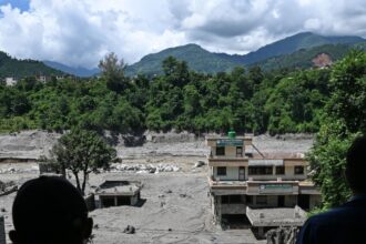 Pessoas em um telhado observam os danos causados ​​por enchentes repentinas em Trishuli, Nepal, na quinta-feira, 27 de agosto.