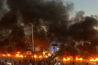 Manifestantes reunidos em rodovia com fumaça ao fundo durante protesto contra o preço dos combustíveis