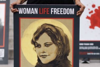 Cartaz de Mahsa Amini, uma iraniana de 22 anos que morreu inesperadamente em 16 de setembro de 2022, sob custódia policial no Irã, após supostamente violar as regras do país sobre o hijab • Dan Kitwood/Getty Images