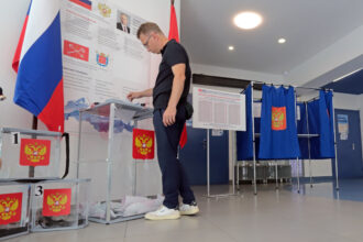 Eleitor deposita voto em urna transparente em seção eleitoral na Rússia