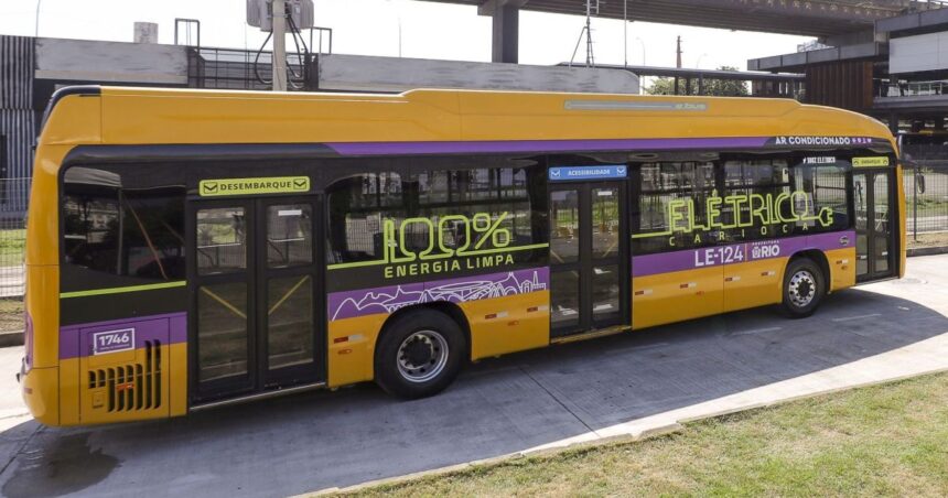 A imagem mostra um ônibus elétrico amarelo, com listras roxas e adesivos com a frase "100% elétrico – energia limpa carioca".