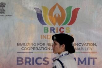 Integrante da Força de Polícia de Reserva Central em frente a um outdoor antes da Cúpula do Brics em Nova Délhi, na Índia