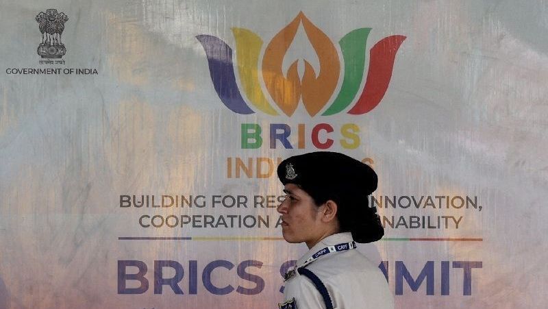 Integrante da Força de Polícia de Reserva Central em frente a um outdoor antes da Cúpula do Brics em Nova Délhi, na Índia