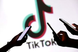 Adolescentes posam para uma foto enquanto seguram smartphones em frente a um logotipo do TikTok nesta ilustração