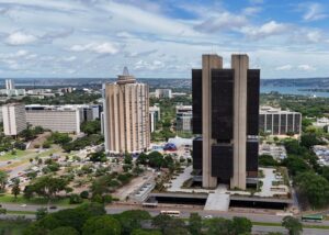 Sede do Banco Central aparece em imagem tirada de longe. O edifíco possui duas colunas brancas e um centro mais escuro, ficando em destqqeu em meio ao resto da cidade que tambpem aparecem na foto
