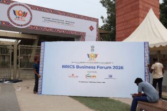 essoas carregam um outdoor do Fórum Empresarial dos Brics 2026 para colocá-lo do lado de fora do Bharat Mandapam, local onde será realizada a 18ª Cúpula dos Brics em Nova Délhi