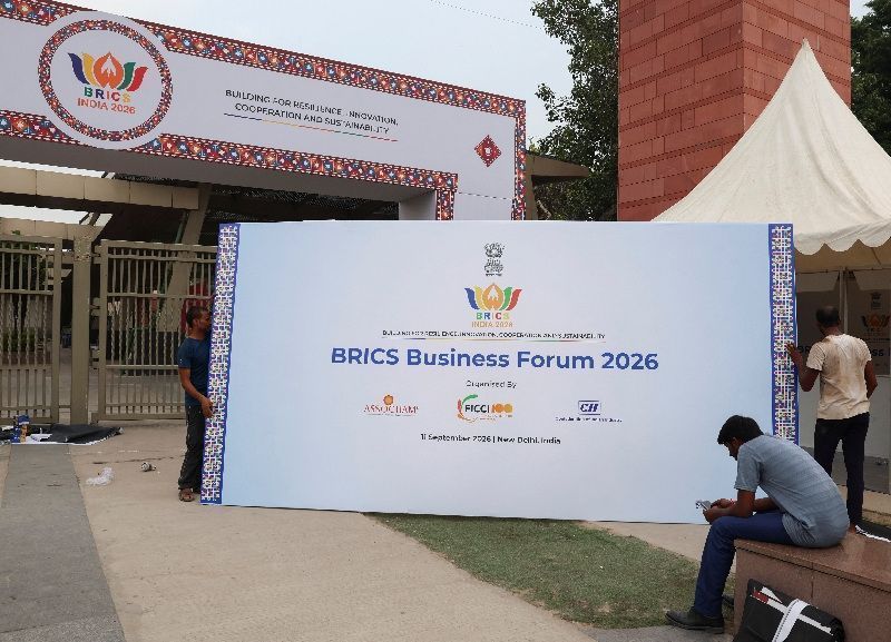 essoas carregam um outdoor do Fórum Empresarial dos Brics 2026 para colocá-lo do lado de fora do Bharat Mandapam, local onde será realizada a 18ª Cúpula dos Brics em Nova Délhi